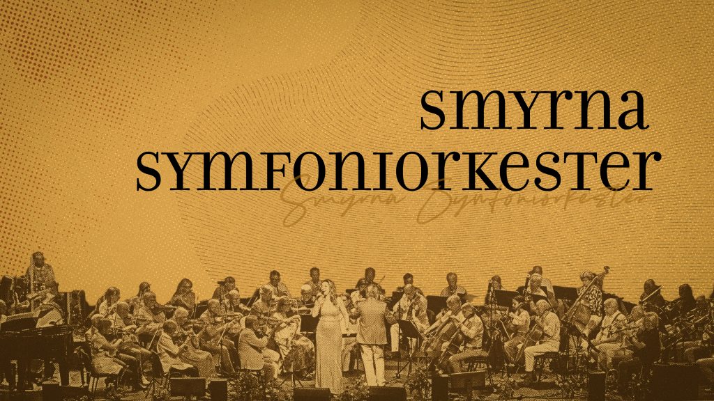 En orkester uppträder på scenen med texten ”Smyrna Symfoniorkester” skriven i stora bokstäver ovanför dem.