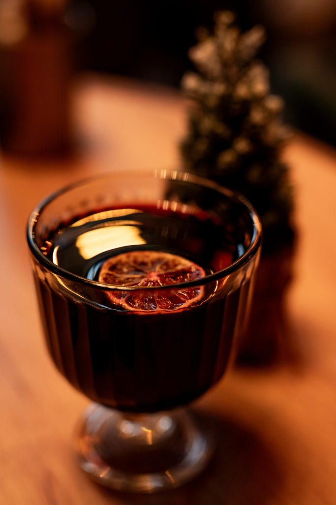 Ett glas glögg garnerat med en torkad apelsinskiva, placerat på en träyta med en suddig bakgrund.