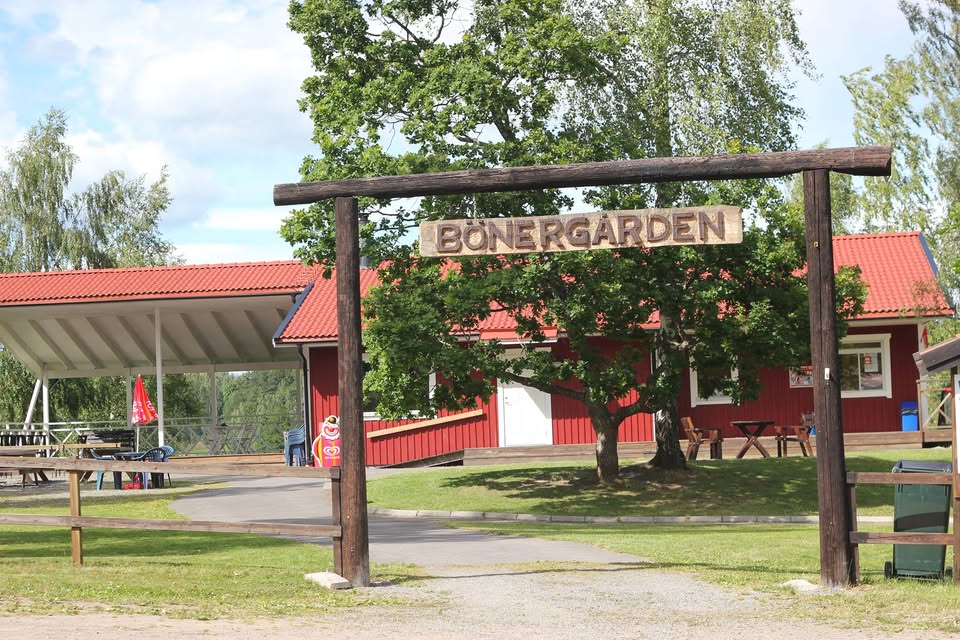 Entrébåge i trä med skylten "BÖNERGÅRDEN", som leder till röda byggnader och ett täckt utomhusområde.
