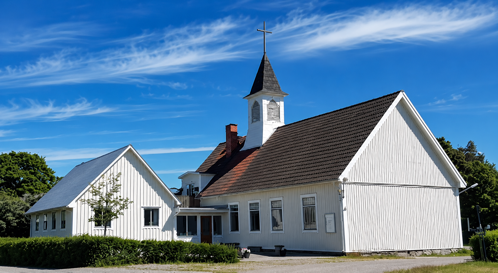 En vit träkyrka med ett torn och ett kors mot en blå himmel med tunna moln.