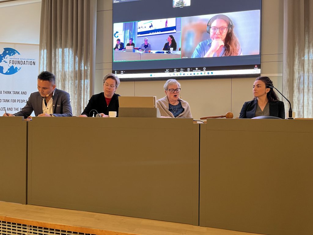 Fyra personer sitter vid ett konferensbord, medan ytterligare tre syns på en stor skärm under ett videosamtal.