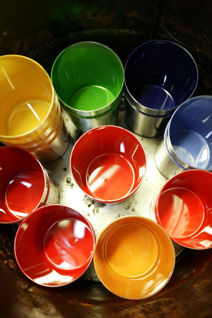 Färgglada plastmuggar uppställda i en cirkel, sedda uppifrån, med röda, gula, gröna och blå muggar.