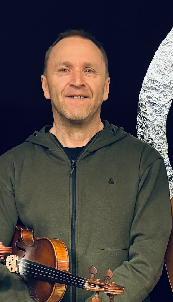 En leende man i en grön huvtröja står mot en mörk bakgrund och håller en fiol i handen.