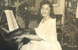 Kvinna i vit klänning ler medan hon spelar piano, med noter och blommor i bakgrunden.