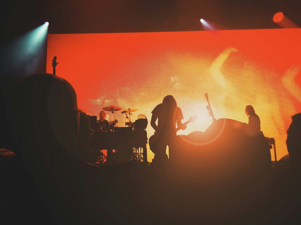 Silhuetter av ett band som uppträder på scenen mot en bakgrund upplyst i orange och rött.