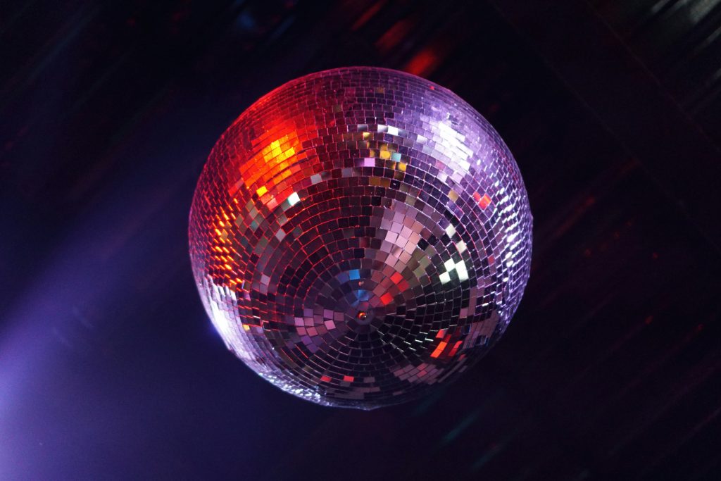 En glänsande discokula som reflekterar röda och lila ljus, hängande från taket i ett mörkt rum.