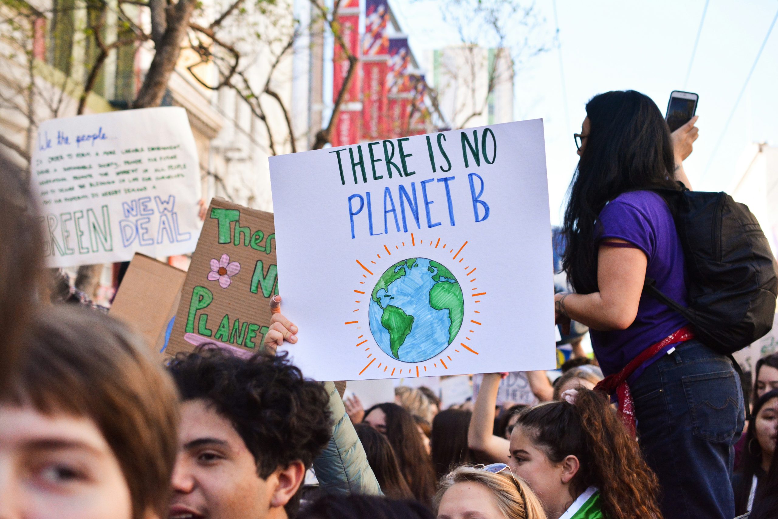 En folkmassa vid en klimatprotest håller skyltar, inklusive en med texten "Det finns ingen planet B" med en jordillustration.