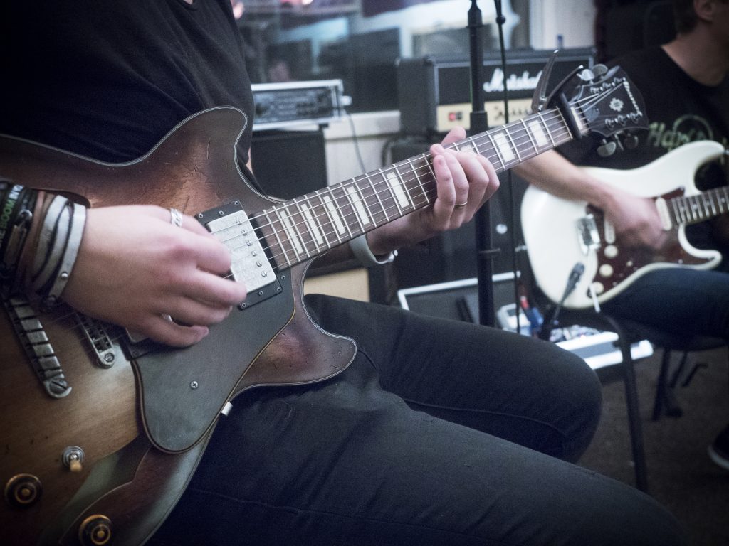 Två personer spelar elgitarr inomhus och fokuserar på sina händer och instrument.