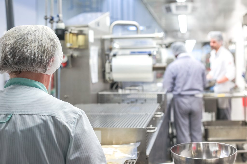 Arbetare i hårnät och uniformer sköter maskinerna i en ren, industriell livsmedelsanläggning.