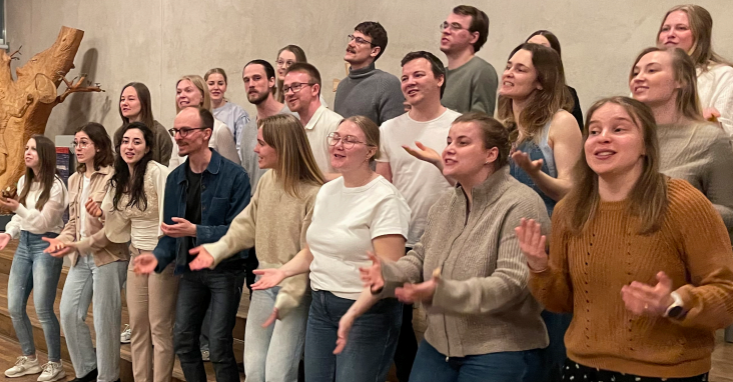En grupp människor som sjunger tillsammans inomhus, ler och gestikulerar med händerna.