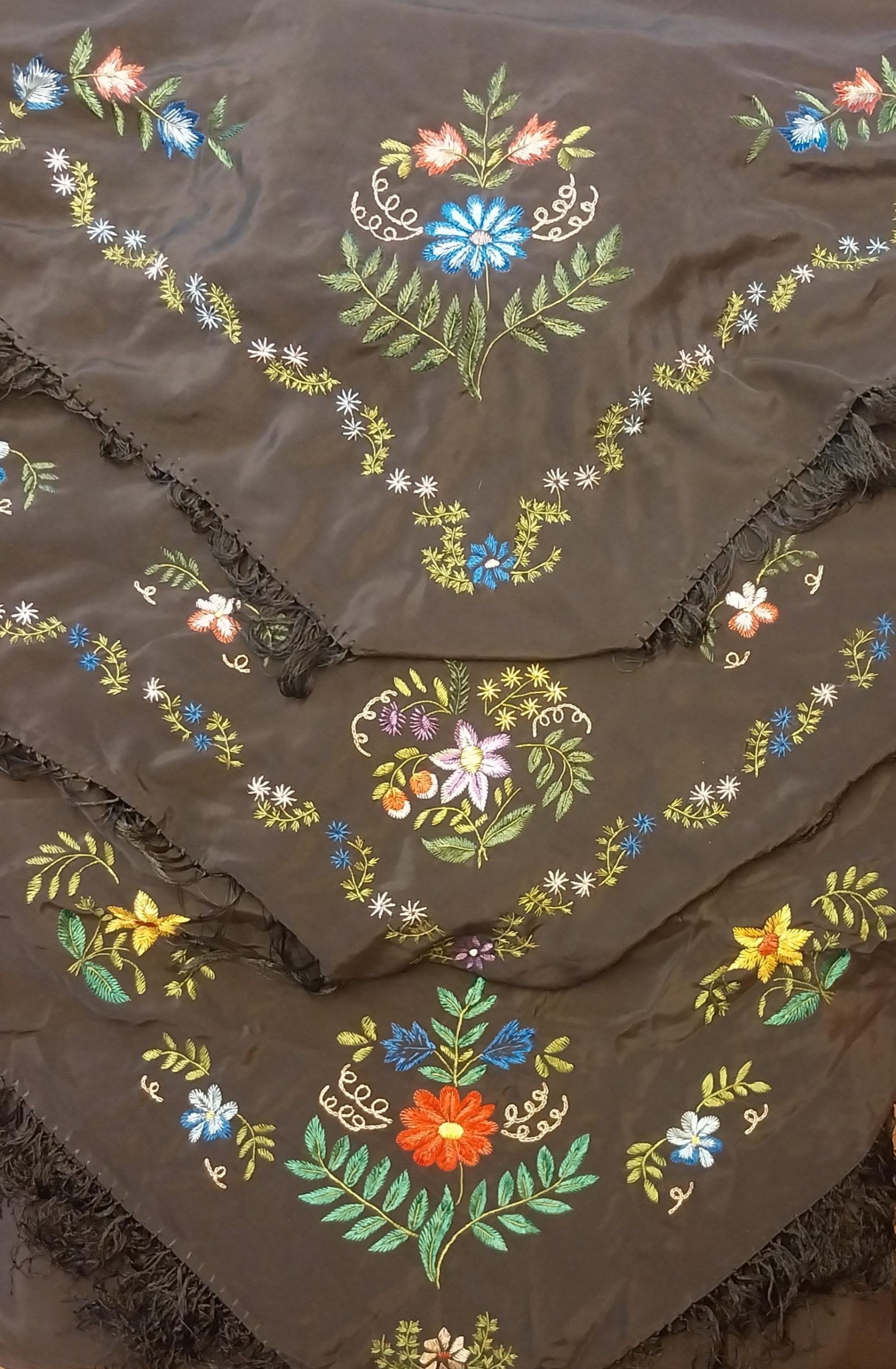 Svarta sidensjalar med färgglada blomsterbroderier och fransade kanter, lagda i lager ovanpå varandra.