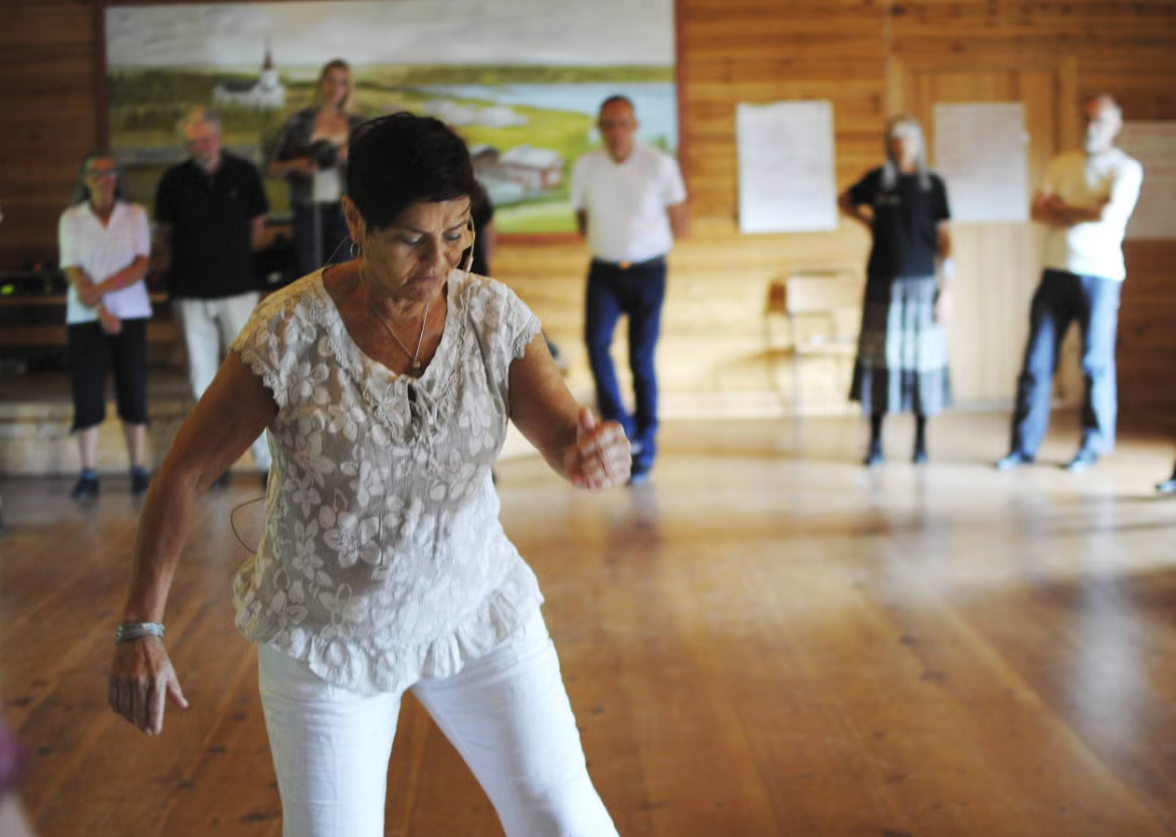 En kvinna som dansar i ett rum med en grupp människor som står i bakgrunden.