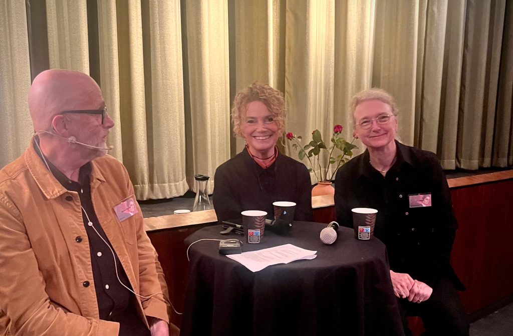 Tre personer som sitter vid ett litet bord under en paneldiskussion.