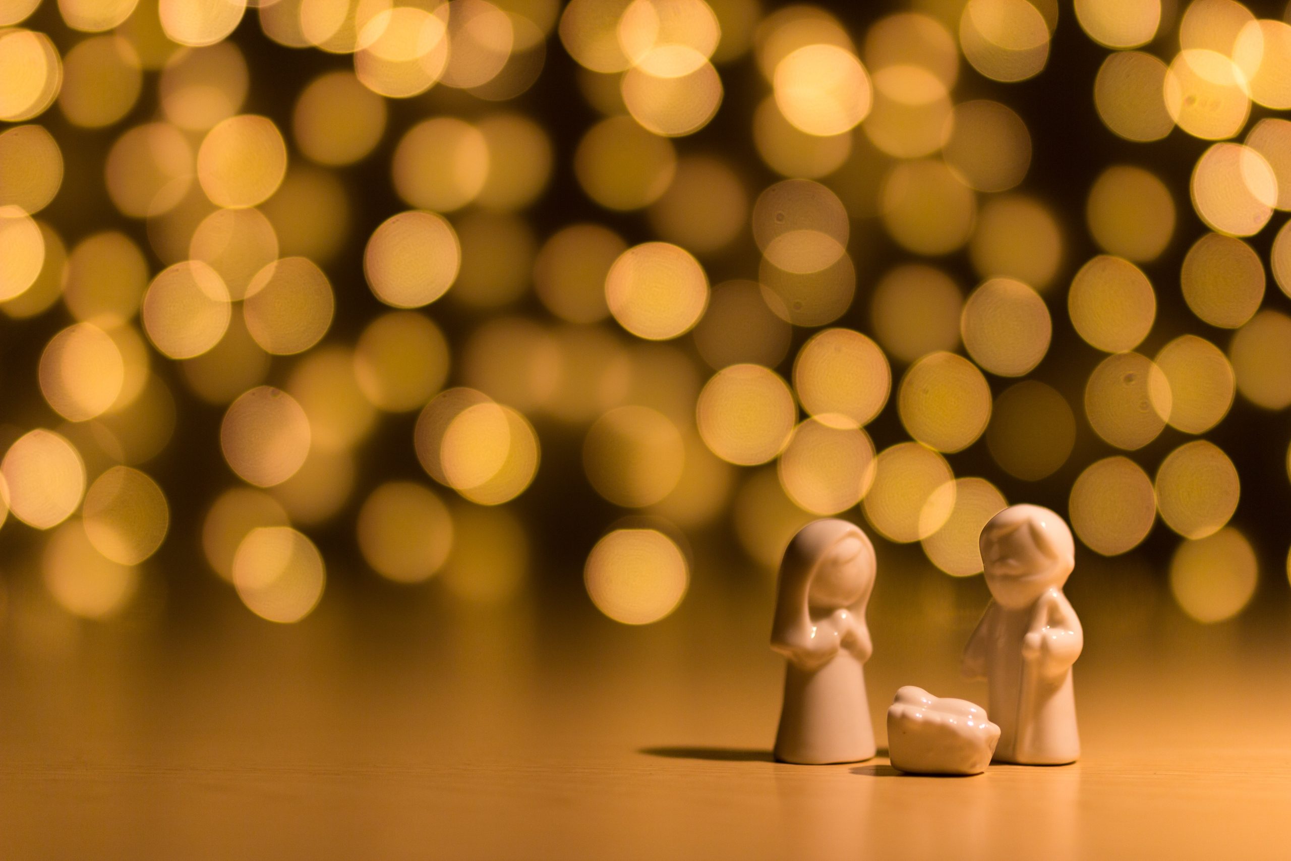 Keramiska julkrubbfigurer föreställande Maria, Josef och Jesusbarnet mot en bakgrund av gyllene ljus.